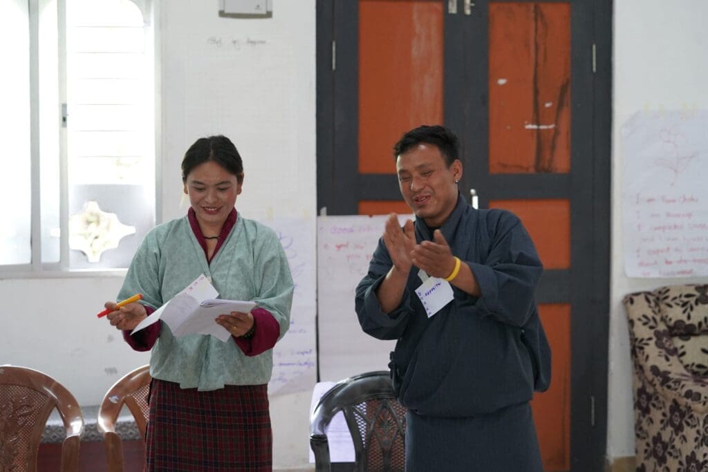 two people pitching their ideas. a smiling man clapping and a women holding a paper of ideas