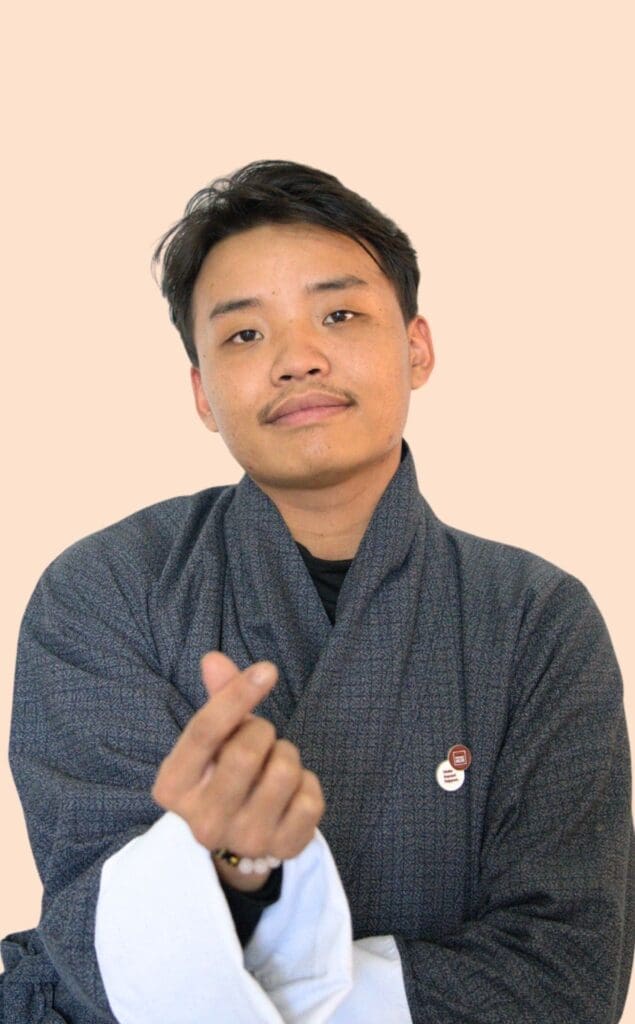 A man wearing Gho and showing love sign is AIDS and Web developer of Impact Hub Thimphu